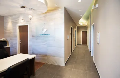 View down a bright, modern hallway in a medical office featuring neutral walls and wooden door frames.
