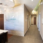 View down a bright, modern hallway in a medical office featuring neutral walls and wooden door frames.