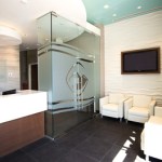 Reception desk and waiting area with white leather armchairs, a wall-mounted TV, and frosted glass walls.