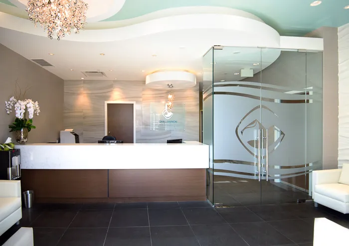 Modern reception waiting area with a front desk, decorative chandelier, and frosted glass entrance doors.