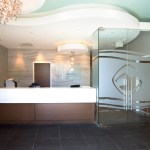 Modern reception waiting area with a front desk, decorative chandelier, and frosted glass entrance doors.