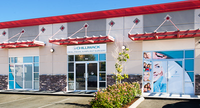 Exterior view of Chilliwack Oral, Facial & Implant Surgery showing the glass entrance and store front beneath a red awning.
