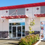 Exterior view of Chilliwack Oral, Facial & Implant Surgery showing the glass entrance and store front beneath a red awning.