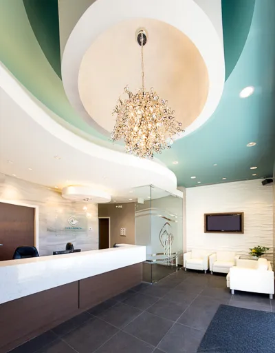 Low-angle view of a bright reception area featuring a large decorative crystal chandelier suspended from a turquoise circular ceiling feature.