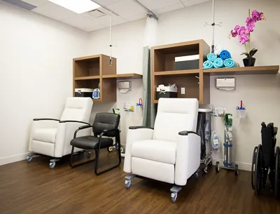 Patient recovery room equipped with two white reclining chairs, medical equipment, storage shelving, and a wheelchair.