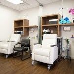 Patient recovery room equipped with two white reclining chairs, medical equipment, storage shelving, and a wheelchair.