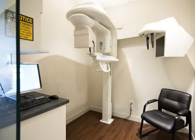 Dental 3D imaging and X-ray room featuring a panoramic CBCT machine, a computer workstation, and a black armchair