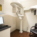 Dental 3D imaging and X-ray room featuring a panoramic CBCT machine, a computer workstation, and a black armchair