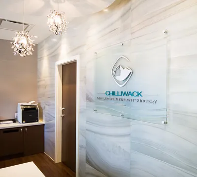 A clear acrylic sign featuring the Chilliwack Oral, Facial & Implant Surgery logo mounted on a marbled wall in an office lobby.