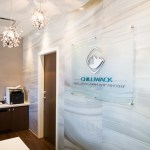 A clear acrylic sign featuring the Chilliwack Oral, Facial & Implant Surgery logo mounted on a marbled wall in an office lobby.