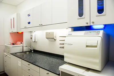 Clean dental sterilization room featuring white cabinetry, a dark countertop sink, and an autoclave machine.